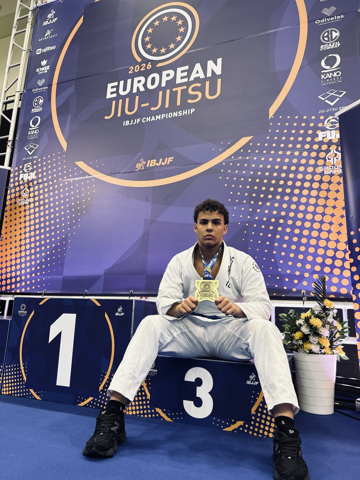 Antonio sentado no pódio do Europeu IBJJF 2026 segurando a medalha